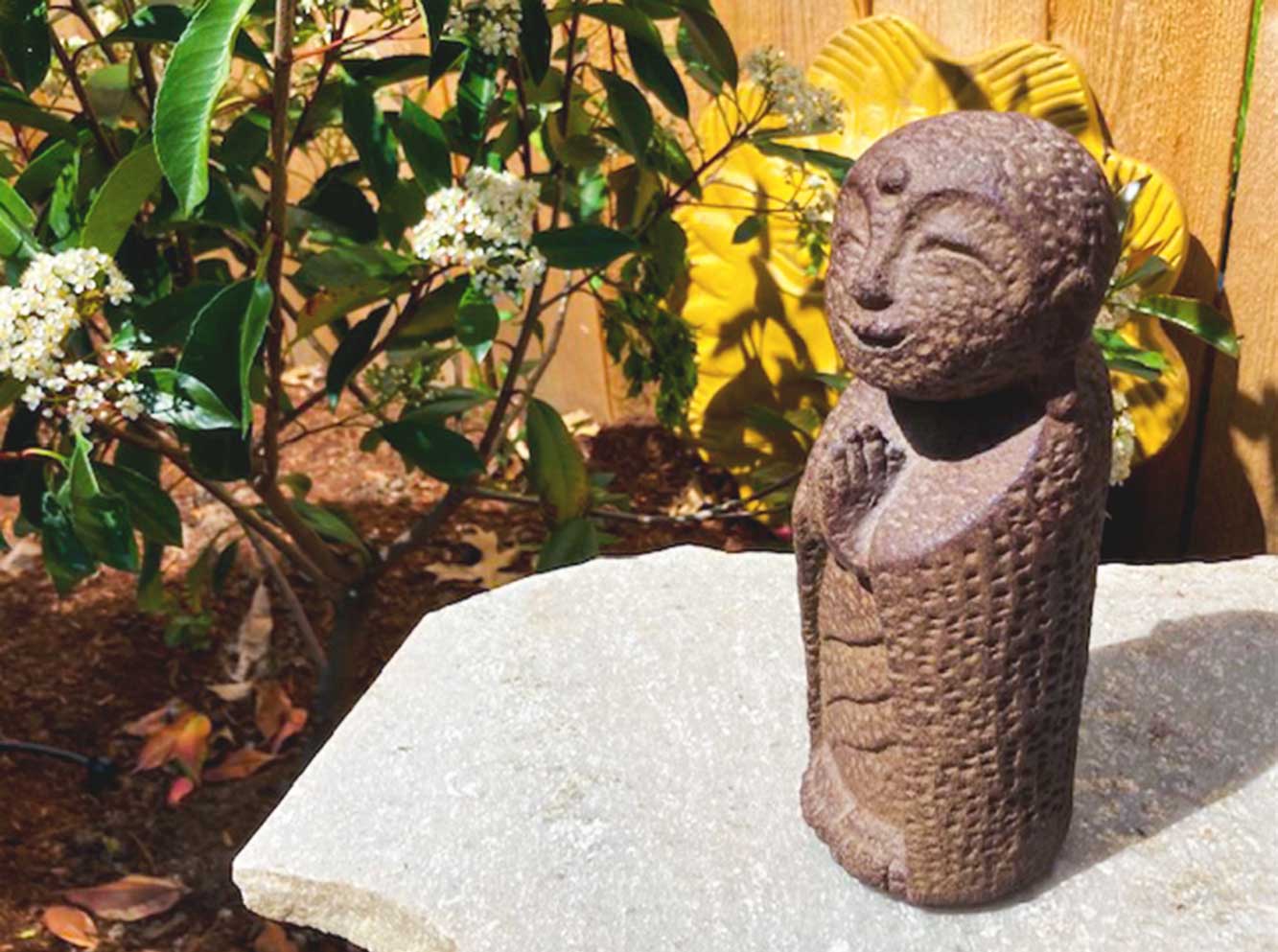 A stone statue of Jizo stands in a garden.